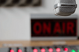 Radio broadcaster’s desk. Mixing board, mic, and “on-air” sign like the old days.