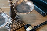 Close-up photo of a scale of justice, a gavel, and books on a wooden surface.
