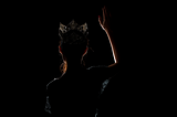 The back of a young beauty pageant contestant standing in the shadowed light wearing the winning crown as she waves to the crowd before her