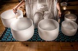 A woman sitting on a mat playing crystal singing bowls