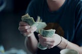 Woman sitting at a table counting cash in her hand.