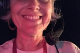 A selfie backstage at a theater of a stage manager on headset. She smiles and wears a white t-shirt.