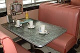 A booth in a dinner complete with three cups, mustard, and a table jukebox.