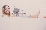 Women laying in bathtub reading a book and smiling.