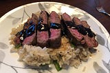 steak slices arranged on a bed of rice with tamari sauce drizzled on top