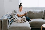 Millennial woman on phone with dog at home.