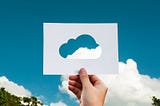 Foto kertas yang berlubang di bagian tengah dengan bentuk awan, serta dihadapkan ke arah langit di mana ada awan sungguhan yang masuk ke dalam lubang kertas tersebut. Mengilustrasikan bahwa artikel ini membahas profesi di bidang cloud computing.