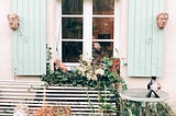 Open shutters on a window with flower box and slatted bench below