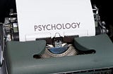 An antique typewriter with a sheet of paper displaying the word Psychology.