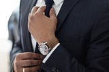 A business man setting his tie, wearing a brown wrist watch