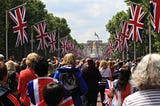 A gaggle of bored british citizens stand in a makeshift queue to nowhere while an endless stream of Union Jacks line an arboreus corridor forcing the crowd’s attention toward the gilded idol that stands before them in the distance.
