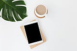 An iPad and Cup of Coffee sit on a desk, beside a plant.