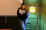Yasmine standing up next to a lamp holding a book.