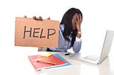 Black woman stressed out in front of her laptop holding a sign that says HELP.