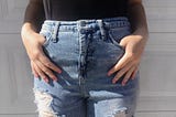 Light blue high-waisted jeans with a few holes in them. Hands in pockets in the front.
