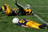 Three young boys playing football, one face down and two others fallen