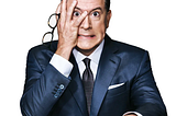 Stephen Colbert has a frustrated angry look on his face as he hides half his face in his hands and holds his glasses. Comedy, Late Show, Colbert, Fallon, democracy, anarchy, shooting in Minneapolis, unrest, law and order, protest