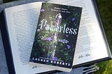 Front of the book Powerless by Lauren Roberts, on top of an open book