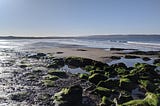 A sandy bay with waves coming in to shore with rock pools in the foreground