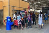 Group of six people crowd around a pop-up vaccination site at a public market.