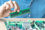 A photo of a man’s hand installing a memory module in a computer’s printed circuit board.