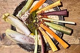 A bowl of hummus and various sticks of vegetables fanned out on top.