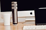 Wooden desk with a white coffee cup, Apple iMac, ipad and Rode Procaster microphone sitting on it.