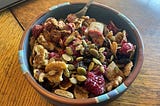 A bowl of whole-grain cereal topped with berries, walnuts, raisins, pumpkin seeds, and cinnamon.