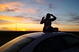 Anne sitting on the roof of her car at sunset