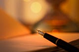 A close-up of a fountain pen resting on an open notebook, softly lit by warm, golden light with a blurred background, evoking a calm and reflective writing atmosphere.