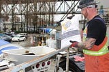 A construction worker is holding a bag of KIM and getting ready to throw it into the ready-mix truck.