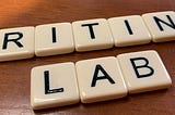 Tile letters from the game “Bananagrams” spell out the words “Writing Lab” on an oak desktop.