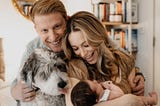 A smiling family with a father, mother, baby, and dog