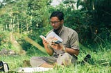 A man sitting on grass, reading a book