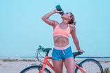 This photo shows a woman taking a break from riding her bike and drinking from her water bottle.