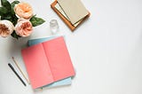 A few sketchbooks rest beside a vase filled with flowers.