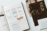 Image of an open planner, calendar, glasses & workspace.