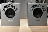 Two speakers on a wood finish table. The one on the left says “ignorance.” The one on the right says “knowledge.” Photo by author, from Virgil Abloh exhibit at The Brooklyn Museum.