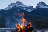 Campfire burning with snow-capped mountain peaks in the distance