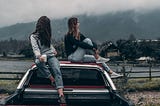 Two women sitting on vehicle roof starring off into the distance