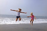 Two extremely joyful little girls, mid-air while jumping simultaneously on the beach.
