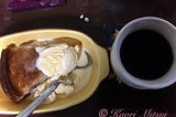 A slice of apple pie with vanilla ice cream on top (left), a cup of black coffee (right)
