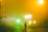 Person with face covered in hoodie walks alone at night with neon lights around them