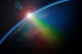 A photo from space of the sun rising over the edge of the earth, creating a rainbow in the ocean.