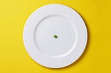 A white plate with a single green pea in the middle