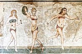 Mosaic portraying three young girls wearing what look like bikinis: one is holding small dumbbells, one is in the act of throwing a discus, the other is running. Two of the girls have blonde hair, the third has brown hair. The discus throwing girl is wearing golden bracelets, necklace and ankle bracelets