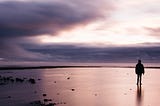 A person on a beach at low tide with clouds on the horizon and on the left