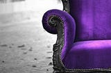 A comfortable, antique purple armchair placed on a cobbled old road.