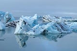 Very icy blue ice bergs floating in a foggy Iceland lagoon, with a beautiful mirror image of the icebergs in the water line.