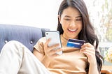 Woman on sofa holding mobile phone and credit card